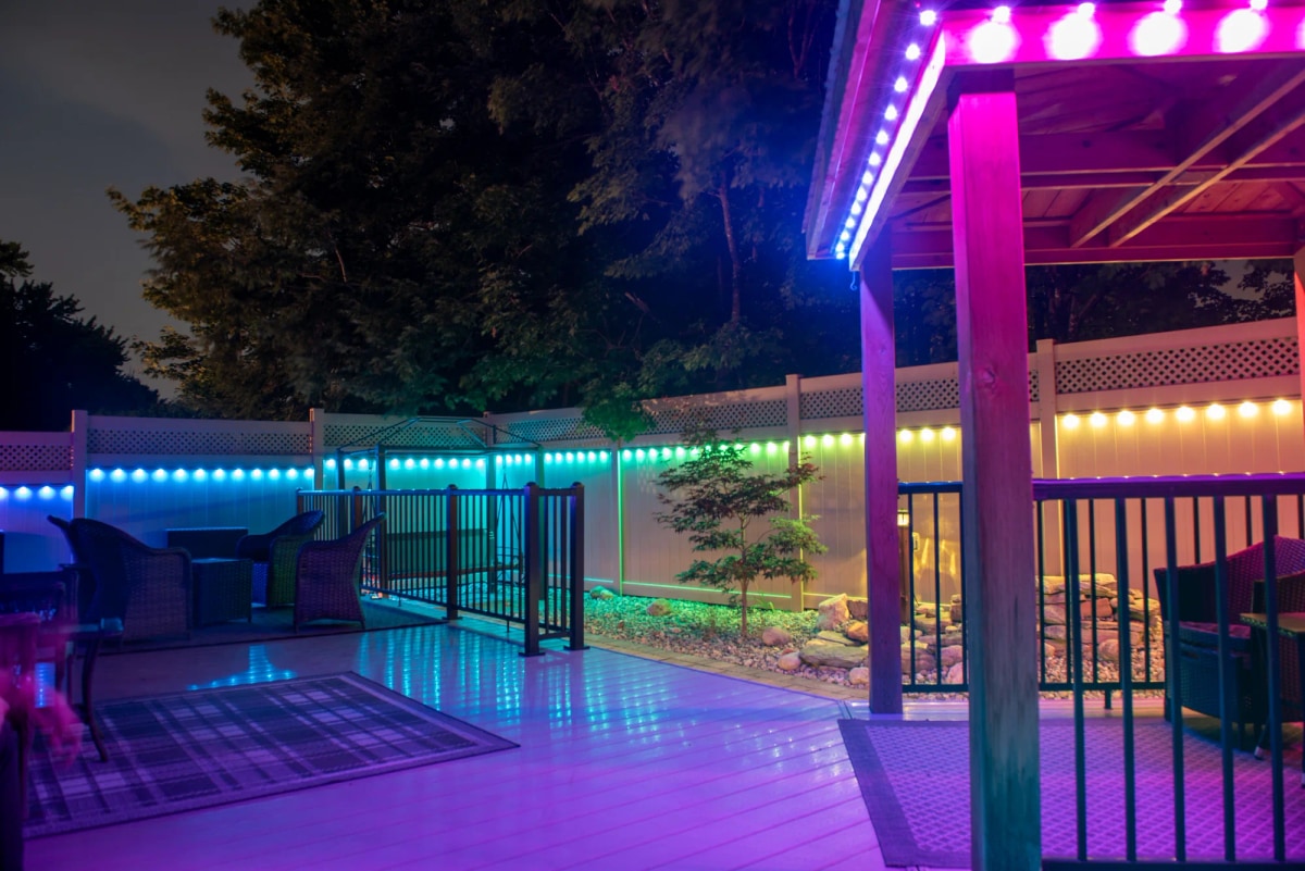 Backyard deck and pergola lit with colorful permanent lighting